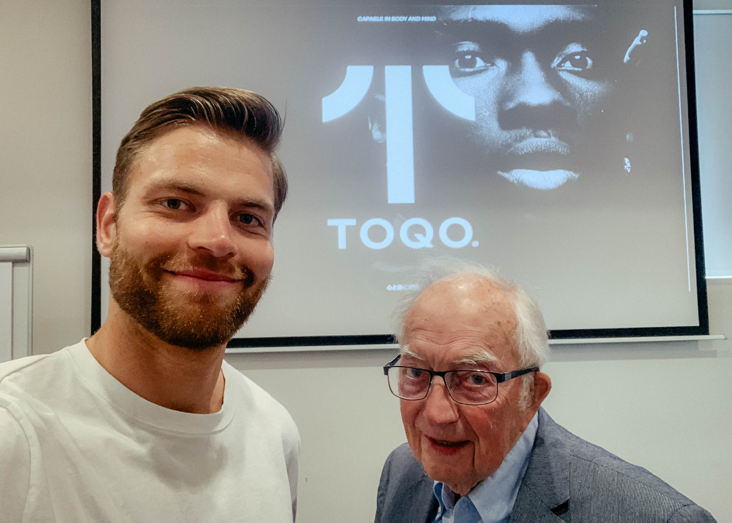 Two men standing in front of the TOQO logo